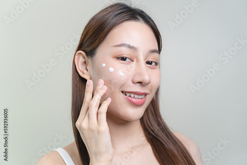 Asian young woman applying cream to her face in routine self care.