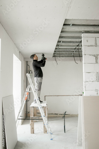 The worker attaches plasterboard on metal frame. Installation of ceiling