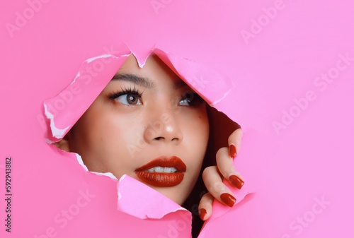 Portrait of beautiful Asian a woman with makeup standing behind pink paper background, copy space.