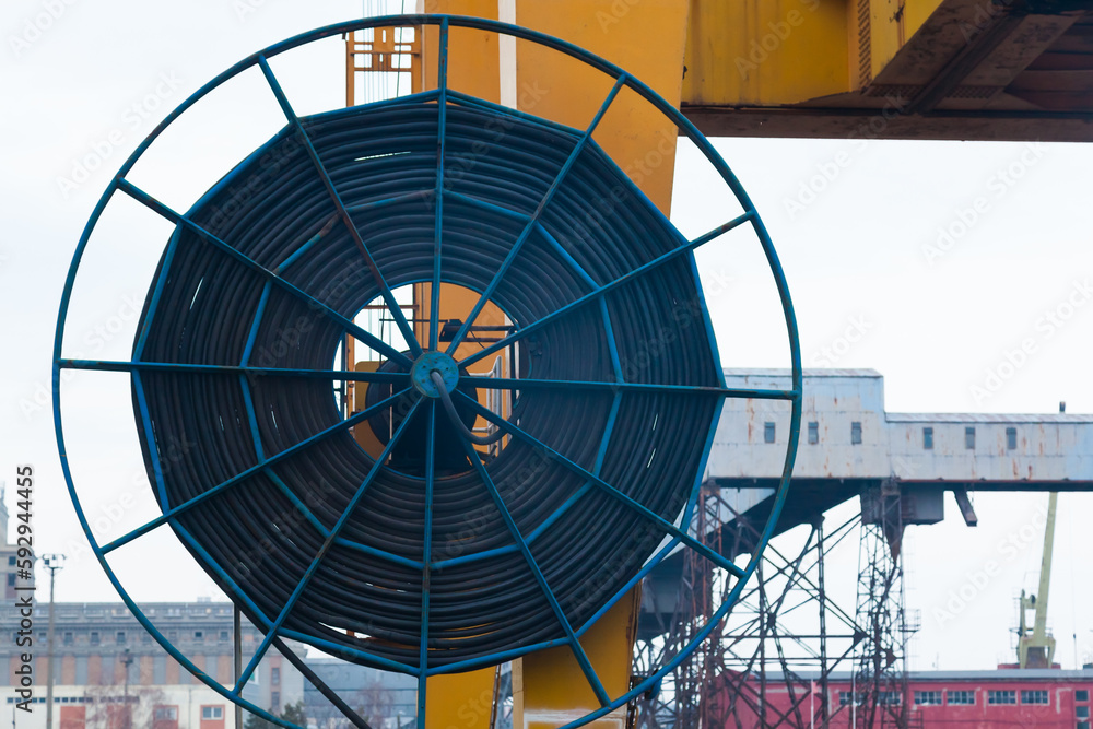 A large wheel with a harbor crane electric cable coiled around it in the port area.