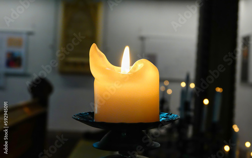 Eine brennende, orangefarbene Kerze auf einem Kerzenhalter aus Metall, in einer Kirche photo