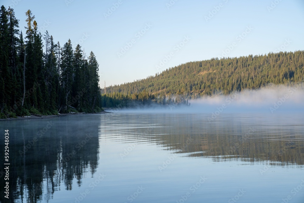 Scenic view of a mountain lake with dense forest covered with fog in the background on a sunny day