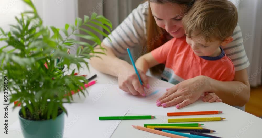Mother and child drawing with pencils sitting at the desk at home. Happy family