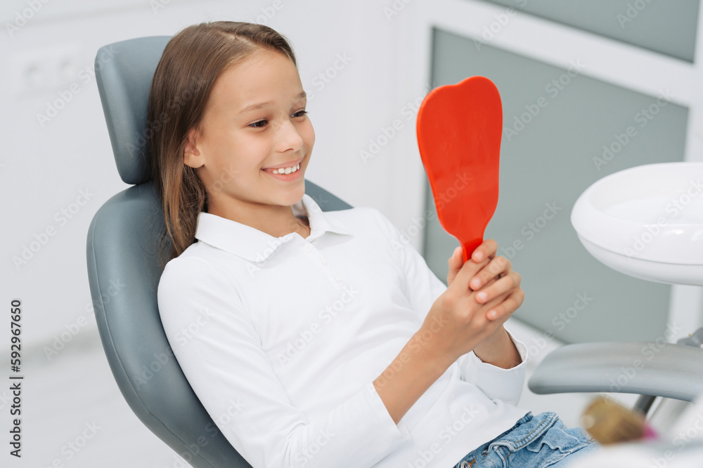 Little patient. A beautiful little girl is smiling and looking in the mirror while sitting in the dentist's office. Dentistry concept Little patient. A beautiful little girl is smiling and looking in the mirror while sitting in the dentist's office. Dentistry concept