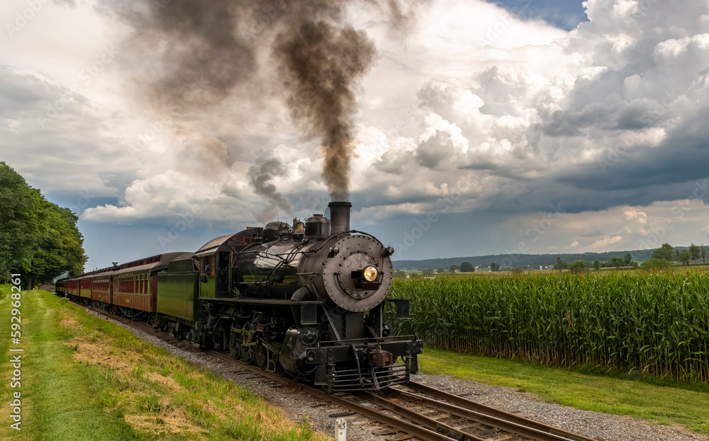 Fototapeta premium Frontal View of Antique Passenger Train Approaching Blowing Black Smoke With Storm Clouds Approaching