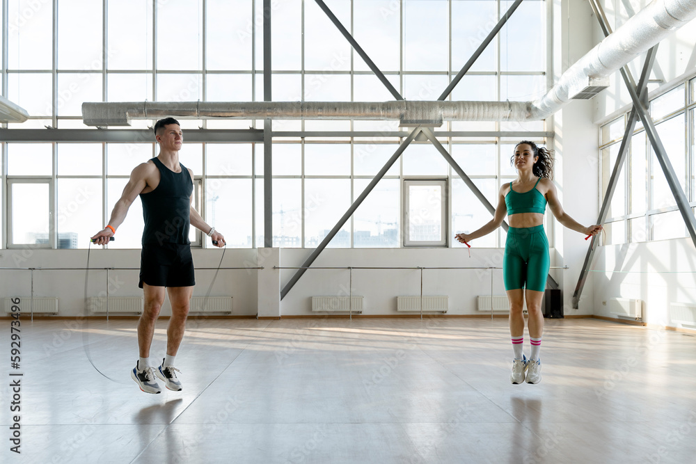 Sporty man and woman perform jumping rope in light sports hall. Сoncept of healthy lifestyle