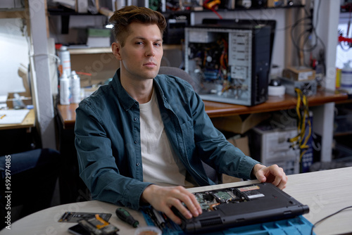 professional young repairman or technician repairs computers and laptop. portrait of service engineer in shirt repairing a laptop, looking at camera seriously, posing, having rest, thinking
