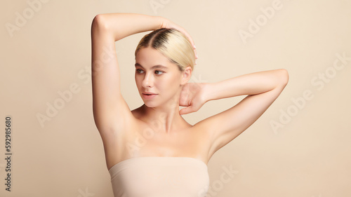 Beautiful Young woman lifting hands up to show off clean and hygienic armpits or underarms on beige background, Smooth armpit cleanliness and protection concept.