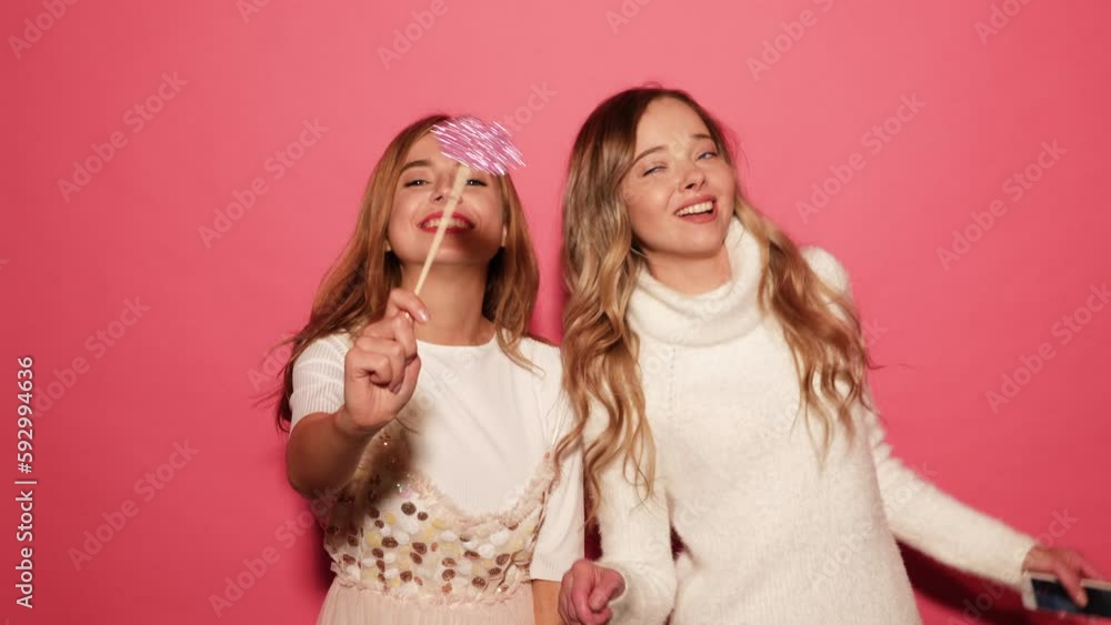 Two beautiful carefree girls. Positive women posing over pink background with paper lips on stick. Female ready for party Two beautiful carefree girls. Positive women posing over pink background with paper lips on stick. Female ready for party