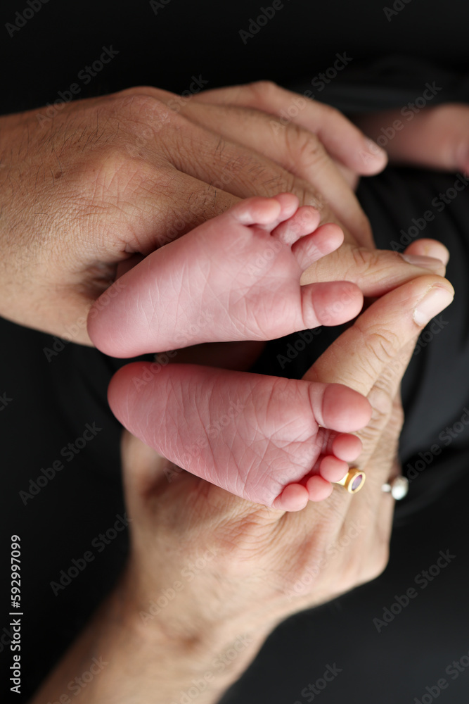 A mother hold the feet of a newborn child in a black blanket on a Black background. The feet of a newborn in the hands of parents. Studio macro photo legs, toes, feet and heels of a newborn.