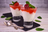 Rice pudding with strawberry jam in glasses on a white wooden background.	