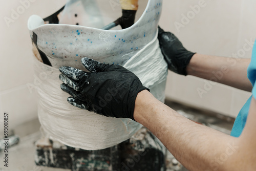 Closeup of crop unrecognizable male worker in black rubber gloves making hip disarticulation prosthesis mold with wet plaster in professional workshop photo