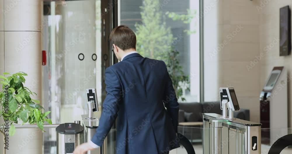 Young businessman in formal suit using electronic keycard, leaving office building, applying identity badge to sensor for gate opening at entrance, walking through business center security equipment Young businessman in formal suit using electronic keycard, leaving office building, applying identity badge to sensor for gate opening at entrance, walking through business center security equipment
