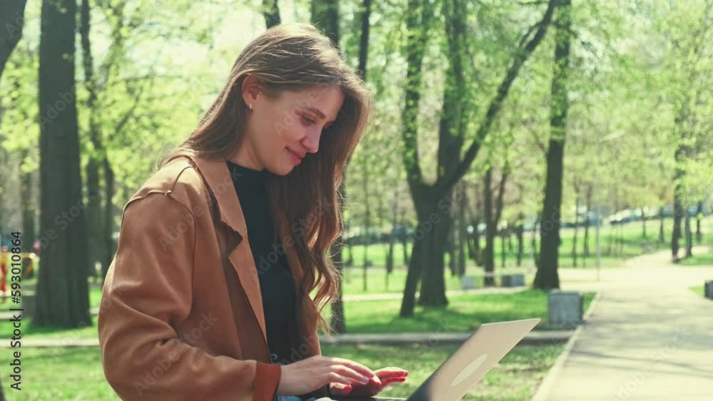 Video of young charming woman sitting in park and working remote on laptop. Video of young charming woman sitting in park and working remote on laptop.