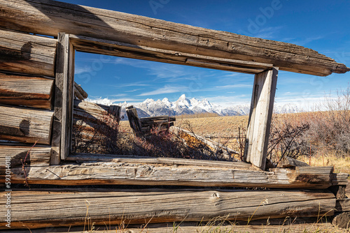 Abandoned deserted log cabin and window to the autumn meadow landscape of Grand Teton Mountain Range in the wilderness area of Wyoming.