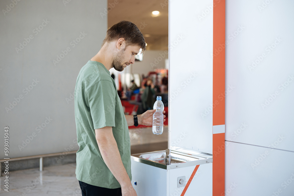 Man refilling his plastic bottle at the airport water fountain. Free public water bottle refill station. Sustainable and green life. Tap refill to reduce plastic bottle usage. Drinking water dispenser Man refilling his plastic bottle at the airport water fountain. Free public water bottle refill station. Sustainable and green life. Tap refill to reduce plastic bottle usage. Drinking water dispenser