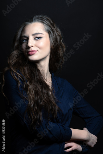 Make-up and fashion concept. Brunette woman with long wavy hair sensual studio portrait. Model wearing blue blouse and looking at camera with blue eyes and seductive look. Toned image with blue color