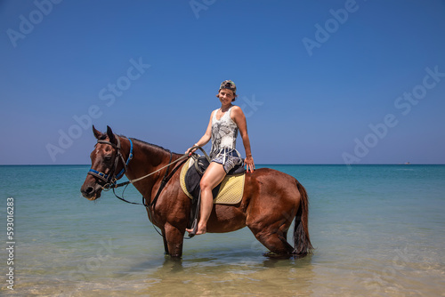 A beautiful girl sits on a horse in the sea. Big beautiful horse. Sunny day. Beautiful beach.