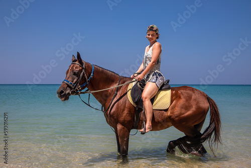 A beautiful girl sits on a horse in the sea. Big beautiful horse. Sunny day. Beautiful beach.