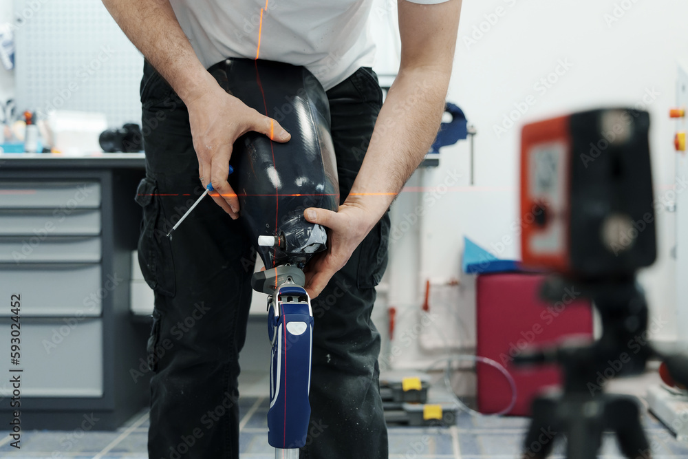 Crop unrecognizable craftsman adjusting and bending modern prosthetic leg at knee section at workbench in manufacturing factory Crop unrecognizable craftsman adjusting and bending modern prosthetic leg at knee section at workbench in manufacturing factory