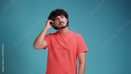 Canvastavla indian man in coral t-shirt on blue studio background thinking pondering looking for an idea