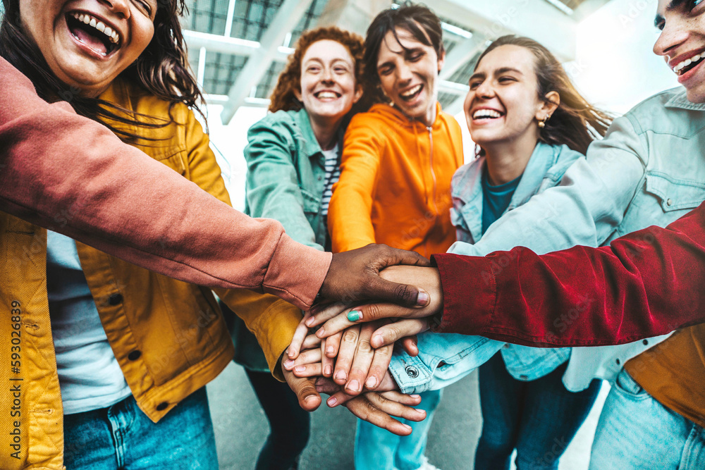 Obraz premium Multiracial group of young people stacking hands outdoors - Happy friends celebrating success on city street - Youth community concept with guys and girls standing together supporting peace and love