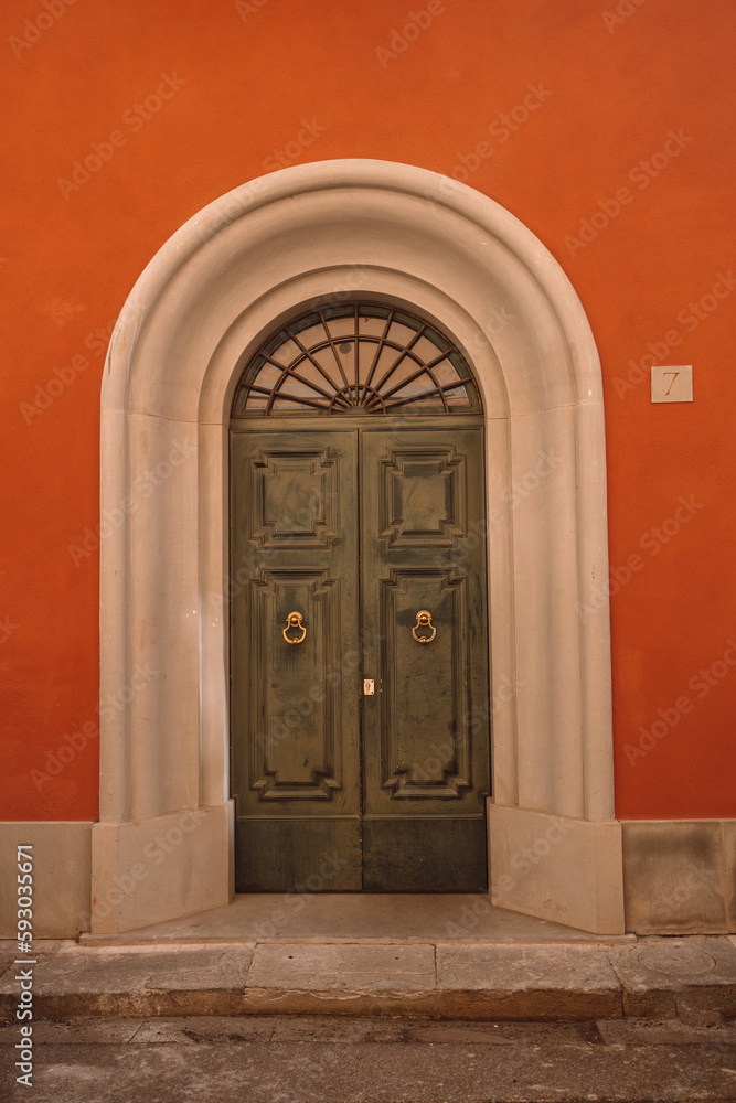 Vintage brown green wooden door with orange wall in Italy
