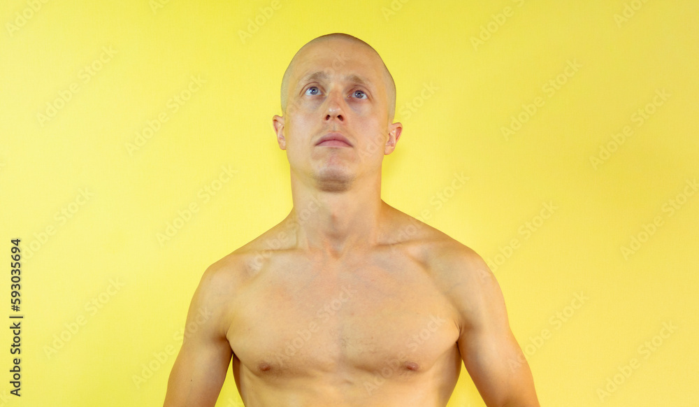 Portrait of a bald athletic young man against a yellow wall. Handsome naked thirty year old man over isolated background. Muscle man
