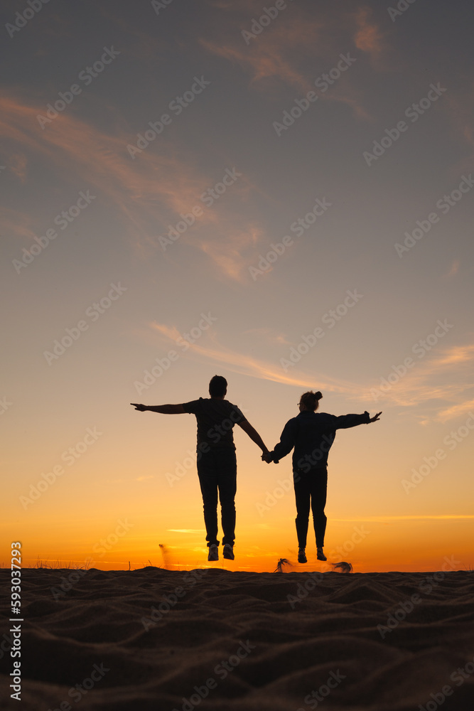 couple of man and woman holding hands jumping on background of the sky. sunset walk on seashore, nature background. joke and fun, relationships and carefree communication