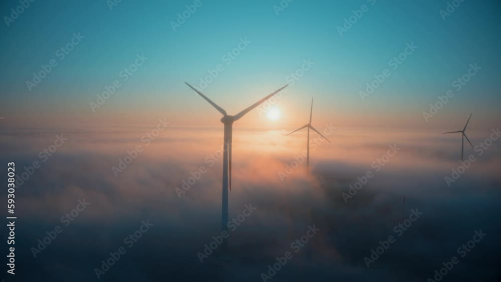 Wind farm at sunrise in heavy fog. Wind turbines generating green energy - concept of renewable electricity, sustainable energy, green power production