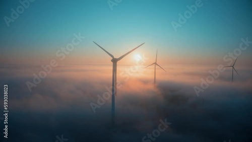 Wind farm at sunrise in heavy fog. Wind turbines generating green energy - concept of renewable electricity, sustainable energy, green power production