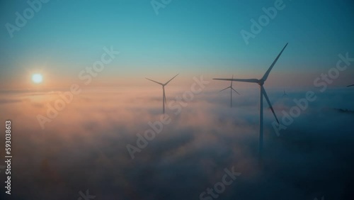 Wind farm at sunrise in heavy fog. Wind turbines generating green energy - concept of renewable electricity, sustainable energy, green power production