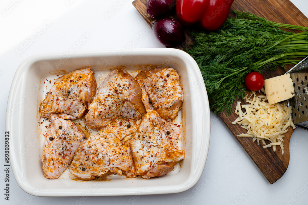 Raw marinated chicken legs in ceramic cooking tray. Fresh vegetables on cutting board Raw marinated chicken legs in ceramic cooking tray. Fresh vegetables on cutting board