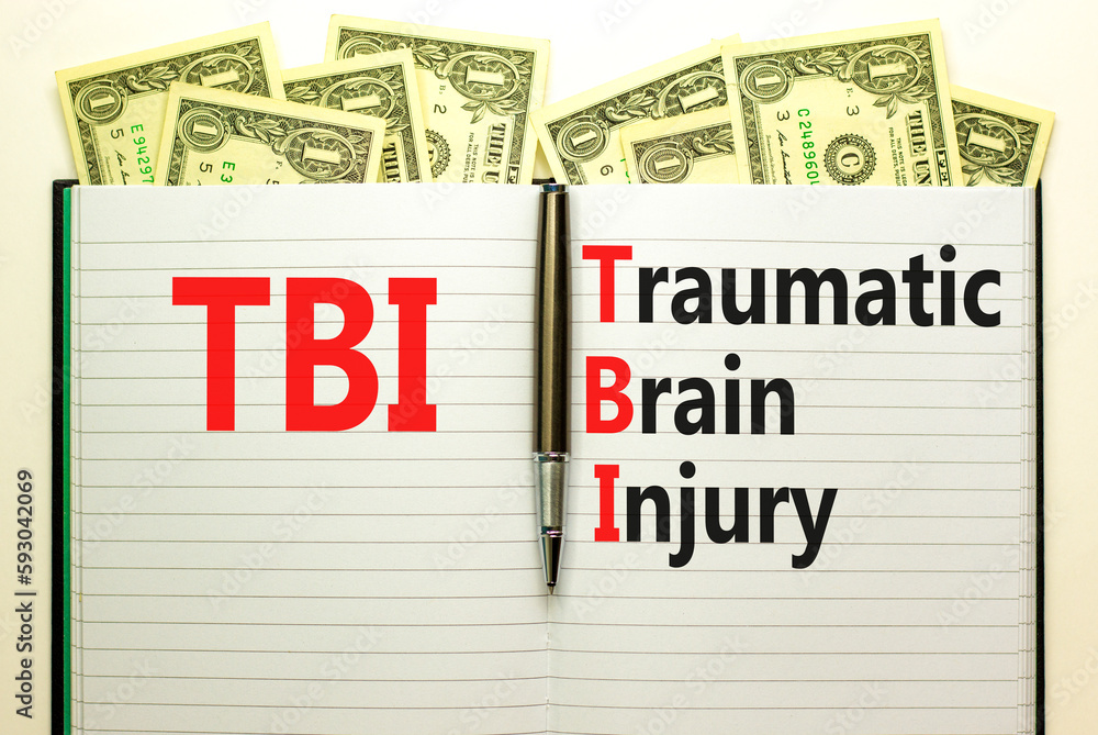 Fototapeta premium TBI traumatic brain injury symbol. Concept words TBI traumatic brain injury on white note on a beautiful background from dollar bills. Pen. Medical and TBI traumatic brain injury concept. Copy space
