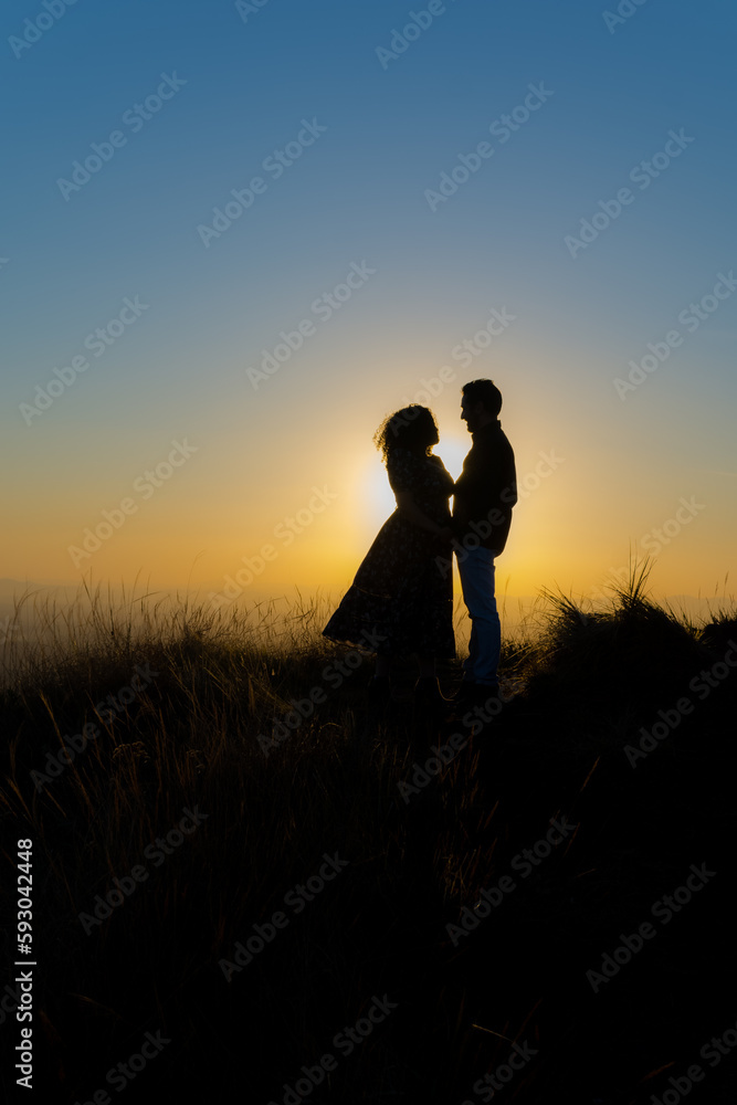 Um casal em contra luz observando o por do sol.