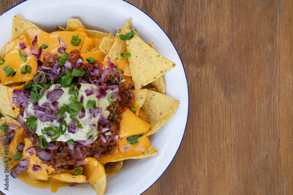 Nachos with chili. Closeup view of nachos with cheddar cheese, avocado cream, red onion pickles and meat sauce in a white bowl. Nachos with chili. Closeup view of nachos with cheddar cheese, avocado cream, red onion pickles and meat sauce in a white bowl.