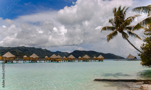 Overwater bungalows stretching out across the lagoon and a few catamarans in a quiet bay in Bora Bora island  Tahiti. Romantic honeymoon destination.