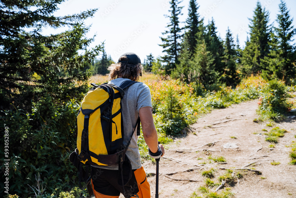 A guy with a backpack in the mountains travels alone, a hipster walks along the trail up to the slope of the summit, a yellow backpack of a climber, equipment for tourism, a hike in the taiga. A guy with a backpack in the mountains travels alone, a hipster walks along the trail up to the slope of the summit, a yellow backpack of a climber, equipment for tourism, a hike in the taiga.