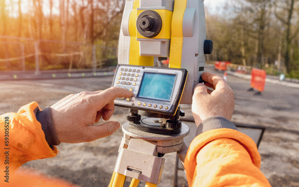 Site engineer operating his instrument during roadworks. Builder using total positioning station tachymeter on construction site for new road setting out - obrazy, fototapety, plakaty 