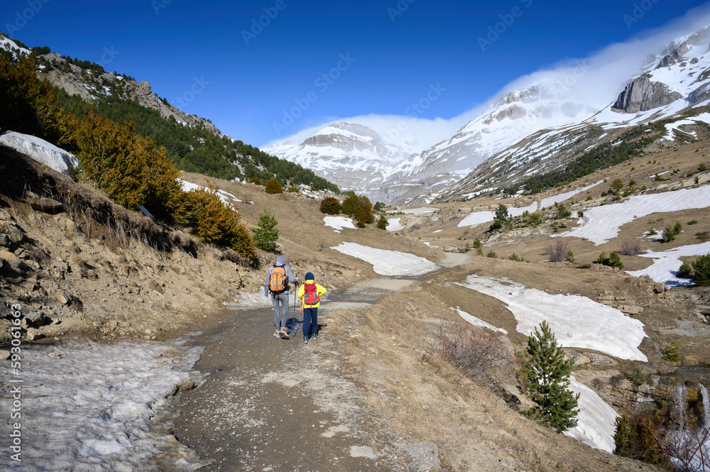 mother and son walking in the snowy mountain next to a river and snowfields. precocious mountain in the pyrenees