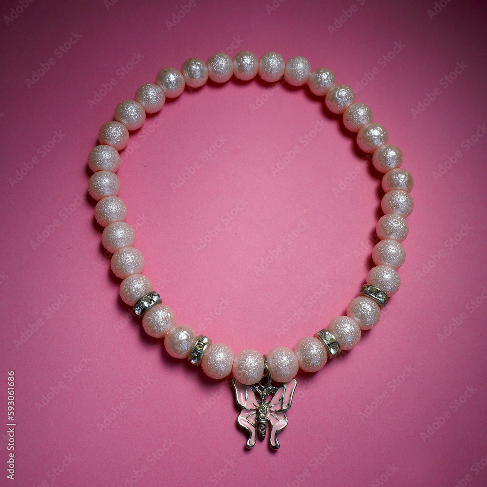 Obraz premium closely made of pink beads with a butterfly pendant a necklace for dogs lies on a pink background. side view . dog accessories gift