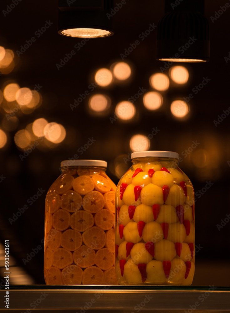 Vertical photo of two isolated bottles (jars) of fruit and vegetables containing orange and pepper standing on a table and on the black blurred background Vertical photo of two isolated bottles (jars) of fruit and vegetables containing orange and pepper standing on a table and on the black blurred background