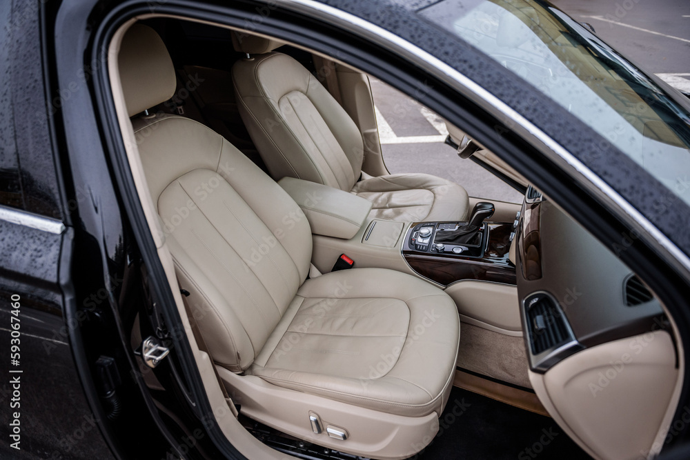 Modern luxury black car standing at parking. Interior of prestige new car. Comfortable perforated beige leather seats. Car detailing series. Side view of the open passenger door, and dashboard of car.