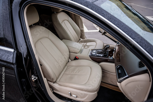 Modern luxury black car standing at parking. Interior of prestige new car. Comfortable perforated beige leather seats. Car detailing series. Side view of the open passenger door, and dashboard of car.