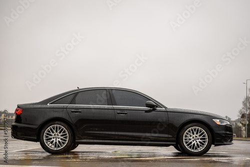 Black new modern business car is parked on the road. Automotive photography. Space for text. Background with car. Side view of the car. Exterior luxury car with tinted glass standing at parking. © Serhii