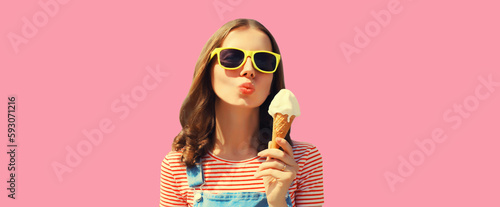 Summer portrait of happy young woman eating ice cream wearing sunglasses on pink background