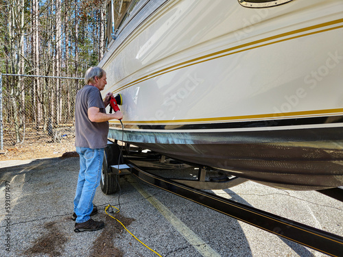 Caucasian man using a portable hand buffing tool on a power boat hull