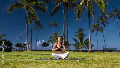 Young woman doing yoga and meditation outside on the grass with palm trees in Hawaii