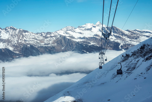 Gondola lifts moving on cables over snow covered hill with beautiful snowcapped Bernese mountains under sky at ski resort in Jungfrau, Switzerland, winter holiday and nature concept