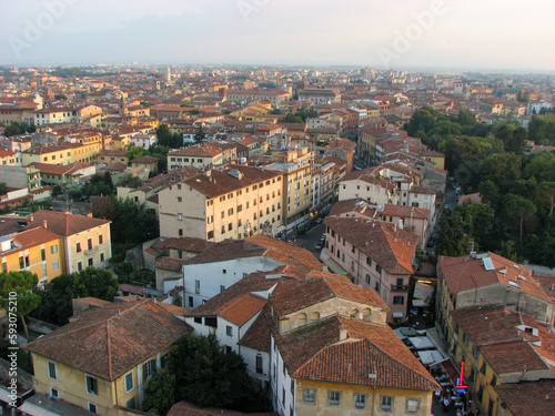 Pisa, Italy - An aerial view from the tower of Pisa's old town, including orange rooftops, in front of a hazy horizon.